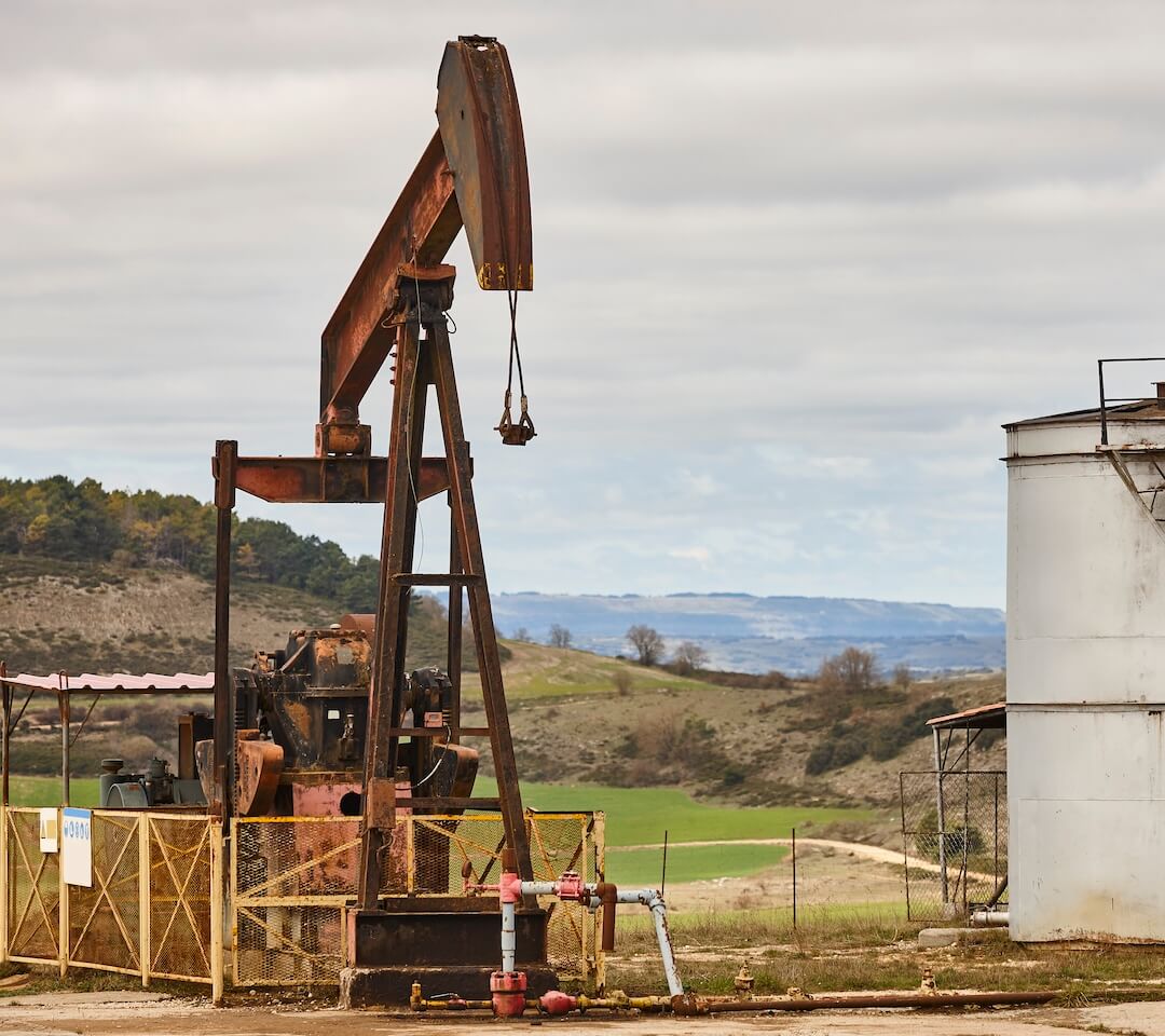 Rusty oil pump jack used for petroleum extraction against a natural landscape.